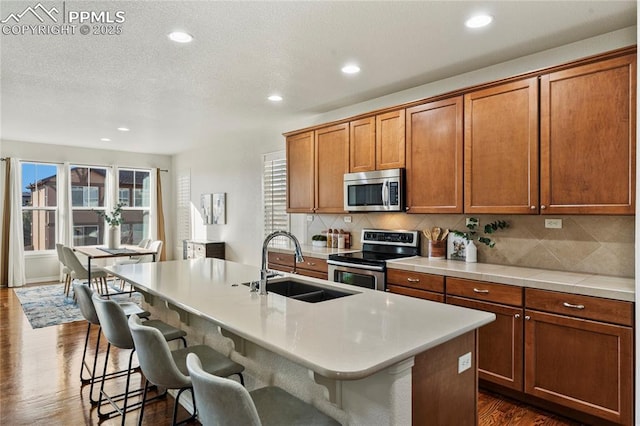 kitchen featuring dark wood-style floors, appliances with stainless steel finishes, brown cabinetry, and a sink