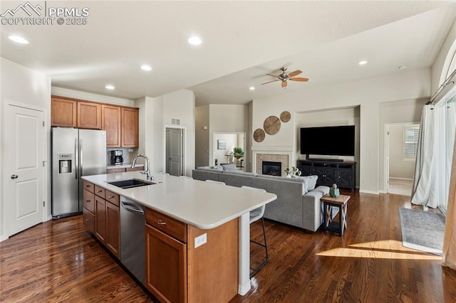 kitchen with an island with sink, a sink, stainless steel appliances, brown cabinetry, and light countertops