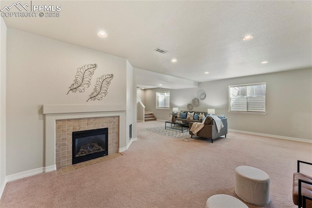 carpeted living room with visible vents, plenty of natural light, a tiled fireplace, and stairway