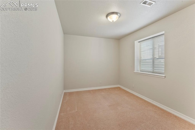 spare room with visible vents, light colored carpet, a textured ceiling, and baseboards