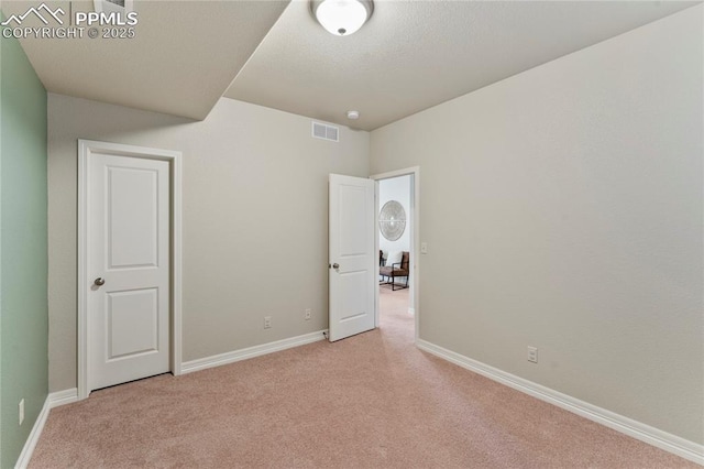 unfurnished bedroom with a textured ceiling, baseboards, visible vents, and light carpet