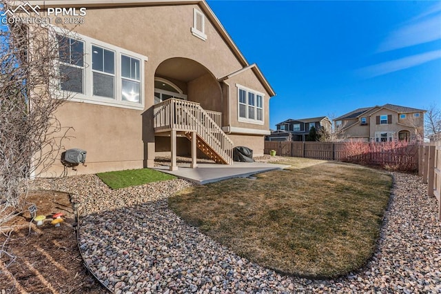 back of house with stucco siding, a lawn, a patio, a fenced backyard, and stairway