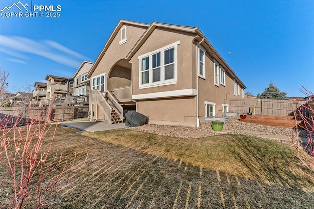 back of property featuring stairway, a fenced backyard, a lawn, and stucco siding