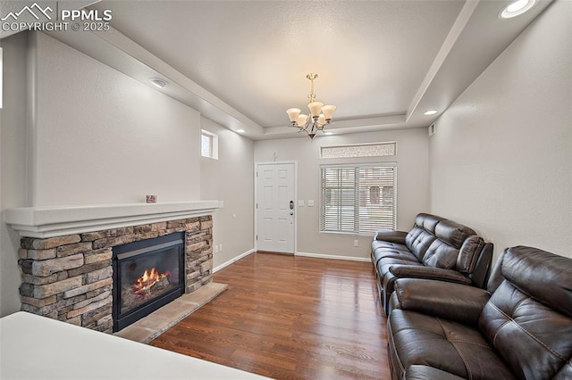 living room with wood finished floors, recessed lighting, an inviting chandelier, baseboards, and a stone fireplace