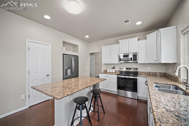 kitchen featuring a breakfast bar area, a sink, stainless steel appliances, white cabinets, and visible vents