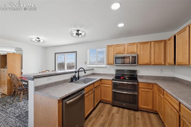 kitchen featuring a peninsula, recessed lighting, a sink, light wood-style floors, and appliances with stainless steel finishes