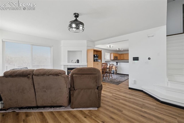 living area featuring a tiled fireplace, light wood finished floors, and baseboards