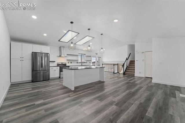 kitchen featuring lofted ceiling with skylight, dark countertops, appliances with stainless steel finishes, wall chimney exhaust hood, and white cabinets