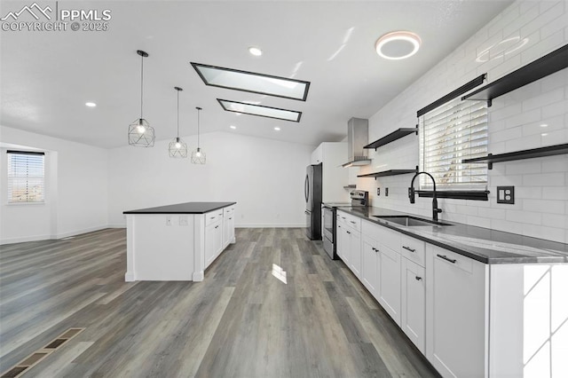 kitchen featuring open shelves, a sink, appliances with stainless steel finishes, dark countertops, and wall chimney exhaust hood