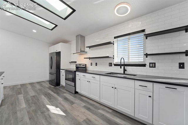 kitchen featuring open shelves, a sink, freestanding refrigerator, stainless steel electric range, and wall chimney range hood