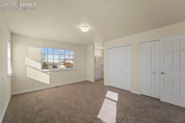 unfurnished bedroom featuring visible vents, two closets, ensuite bathroom, carpet flooring, and baseboards