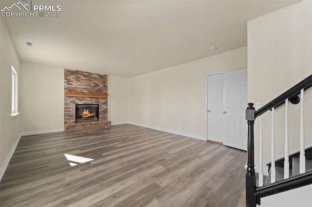 unfurnished living room with stairway, baseboards, visible vents, and wood finished floors