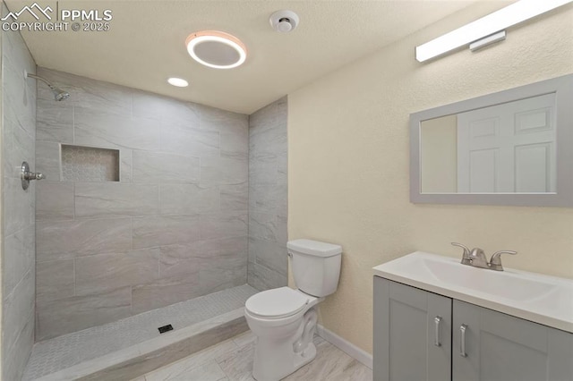 bathroom featuring vanity, toilet, baseboards, and a tile shower