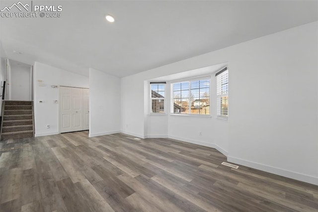 empty room featuring stairway, baseboards, visible vents, dark wood finished floors, and lofted ceiling