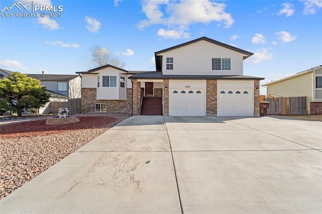 tri-level home featuring brick siding, an attached garage, concrete driveway, and fence