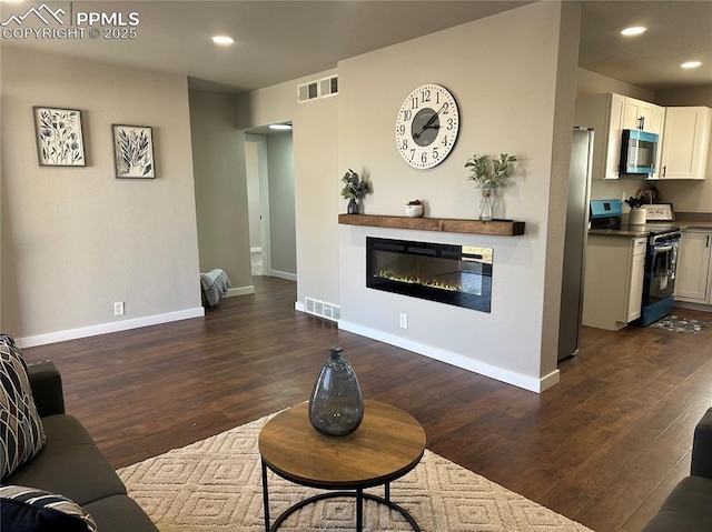 living room with a glass covered fireplace, dark wood-type flooring, visible vents, and baseboards