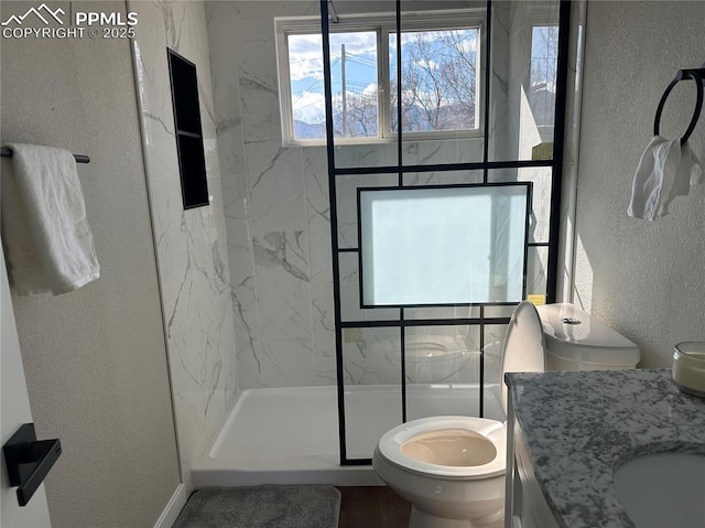 bathroom with a marble finish shower, toilet, vanity, and a textured wall