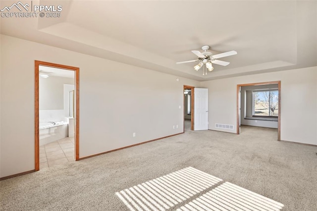 unfurnished bedroom featuring carpet, visible vents, baseboards, ensuite bathroom, and a raised ceiling