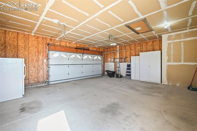 garage with wood walls, a garage door opener, and freestanding refrigerator