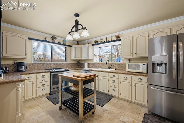 kitchen with a sink, decorative light fixtures, cream cabinets, appliances with stainless steel finishes, and crown molding