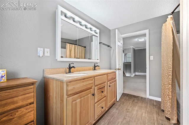 full bathroom with a textured ceiling, double vanity, wood finished floors, and a sink