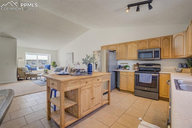 kitchen with light brown cabinets, open floor plan, light countertops, lofted ceiling, and appliances with stainless steel finishes