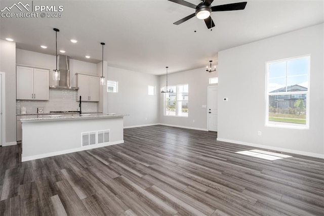 unfurnished living room featuring baseboards, visible vents, recessed lighting, dark wood-style flooring, and ceiling fan with notable chandelier