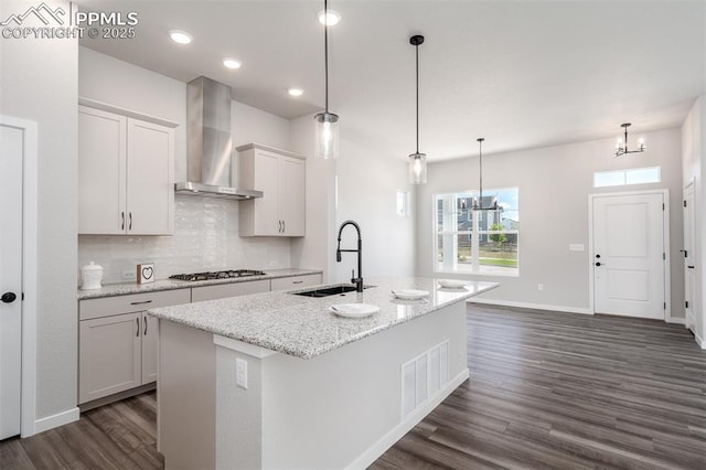 kitchen featuring visible vents, a sink, dark wood-type flooring, wall chimney range hood, and a chandelier