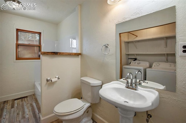 full bath with visible vents, toilet, washer and clothes dryer, a sink, and wood finished floors