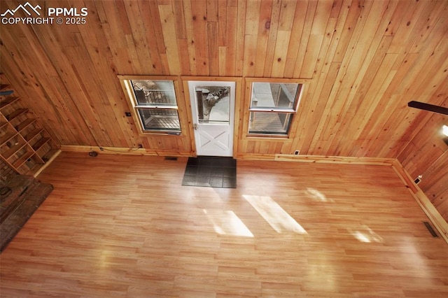 spare room with wooden walls, light wood-style floors, visible vents, and baseboards