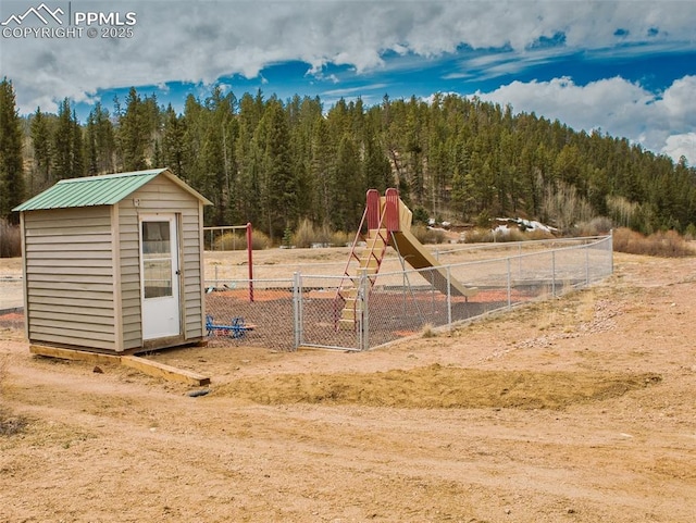 view of playground with a forest view, a storage shed, an outdoor structure, and fence