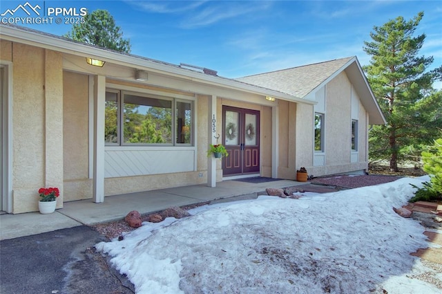 doorway to property featuring stucco siding and roof with shingles