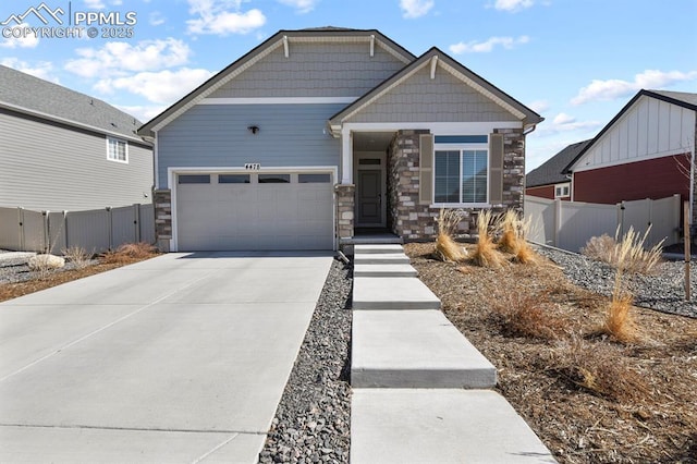 craftsman-style house featuring stone siding, an attached garage, concrete driveway, and fence