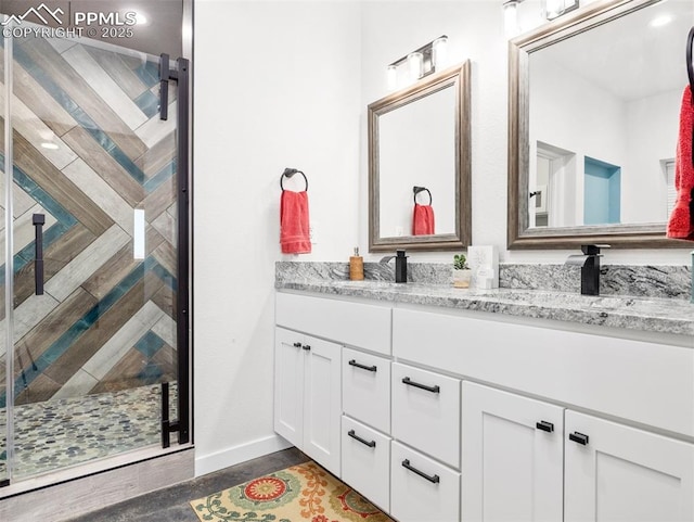 bathroom with double vanity, baseboards, a shower stall, and a sink