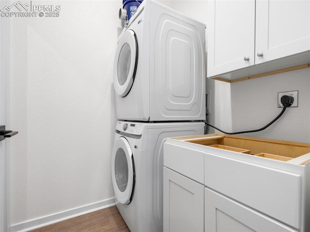 washroom featuring cabinet space, stacked washing maching and dryer, baseboards, and wood finished floors