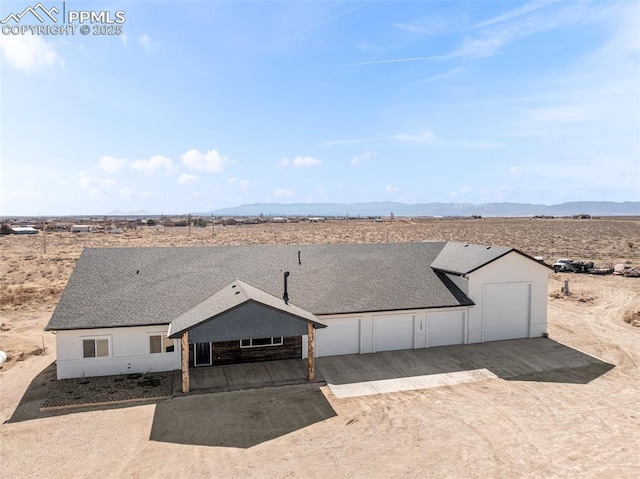 rear view of house featuring a mountain view, view of desert, driveway, and a shingled roof