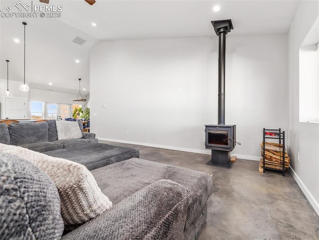 interior space with baseboards, visible vents, a wood stove, ceiling fan, and vaulted ceiling