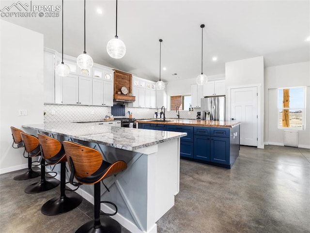 kitchen featuring finished concrete flooring, white cabinets, stainless steel fridge, blue cabinets, and a sink