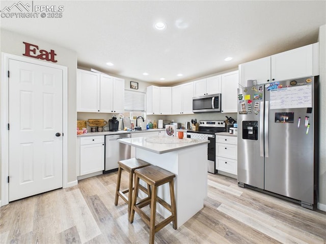 kitchen with a sink, light countertops, white cabinets, light wood-style floors, and appliances with stainless steel finishes