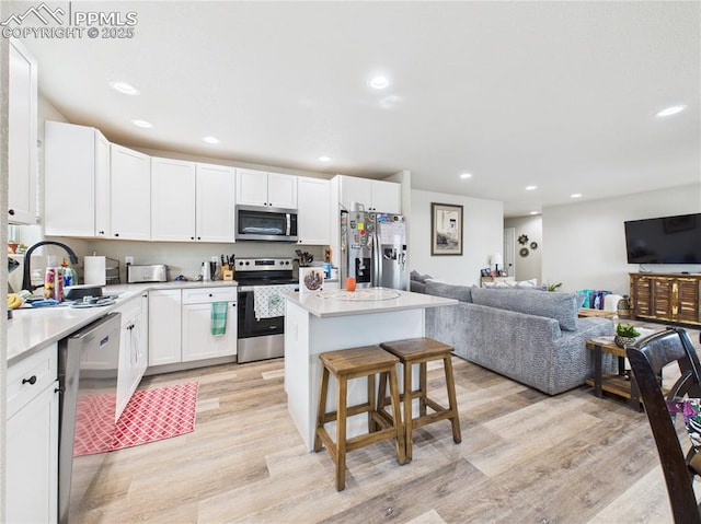 kitchen featuring stainless steel appliances, open floor plan, a kitchen bar, light wood-type flooring, and a center island