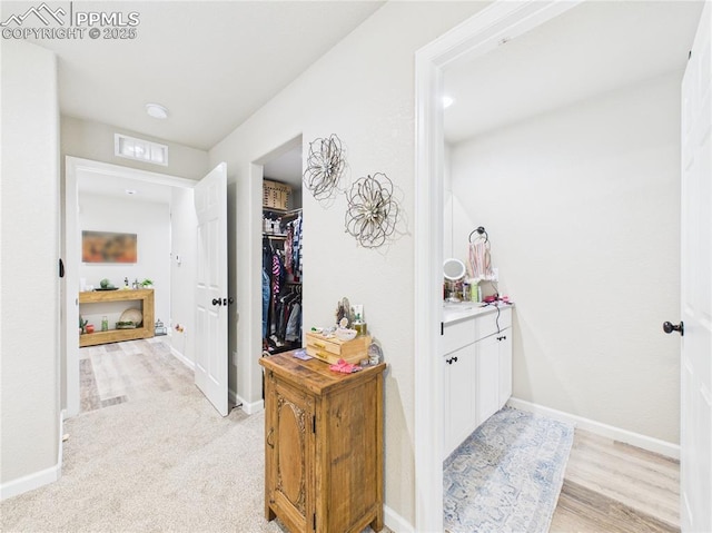 hall featuring light wood-style flooring, baseboards, and visible vents