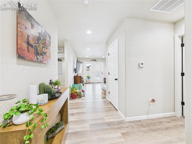 corridor featuring visible vents, a textured ceiling, wood finished floors, baseboards, and a textured wall