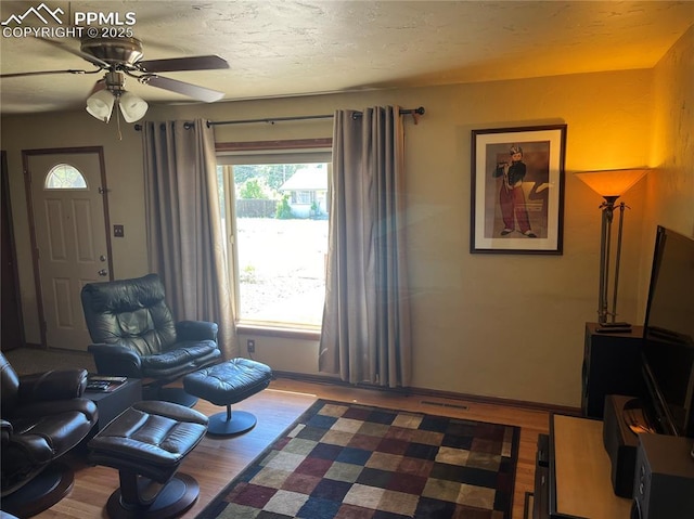 living area with visible vents, ceiling fan, baseboards, wood finished floors, and a textured ceiling