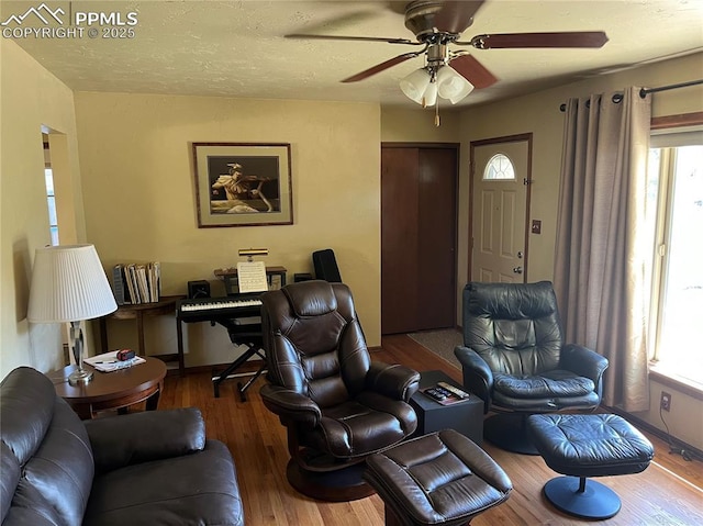 living area with ceiling fan, baseboards, a textured ceiling, and wood finished floors