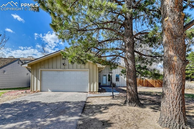 view of front of home featuring board and batten siding, driveway, fence, and an attached garage