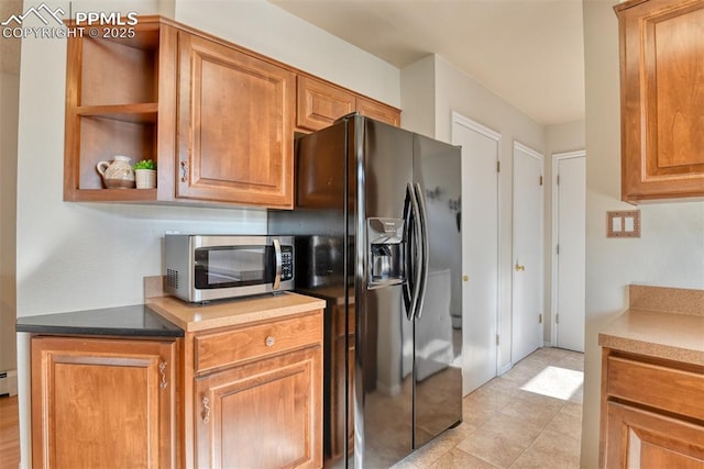 kitchen featuring stainless steel microwave, black fridge with ice dispenser, brown cabinetry, and open shelves