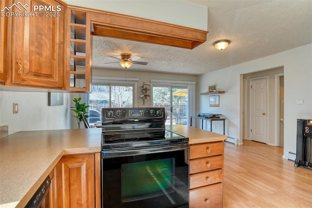 kitchen featuring light countertops, light wood-style flooring, a ceiling fan, black range with electric stovetop, and brown cabinetry