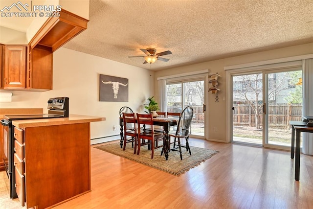 dining space with light wood-type flooring, ceiling fan, a baseboard heating unit, and a textured ceiling