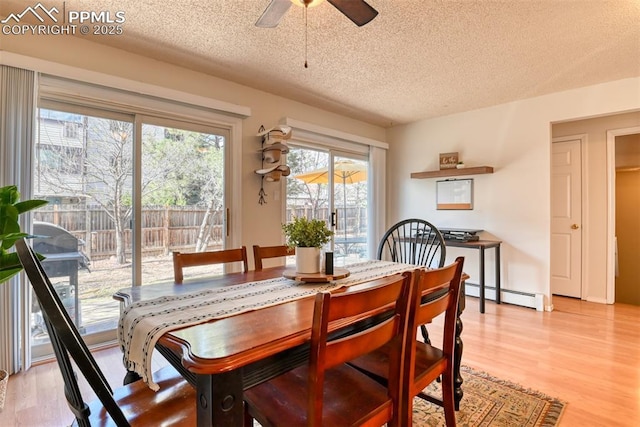 dining area with light wood finished floors, ceiling fan, a baseboard heating unit, and a textured ceiling