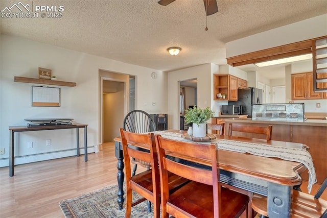 dining area featuring light wood finished floors, a textured ceiling, baseboard heating, and a ceiling fan